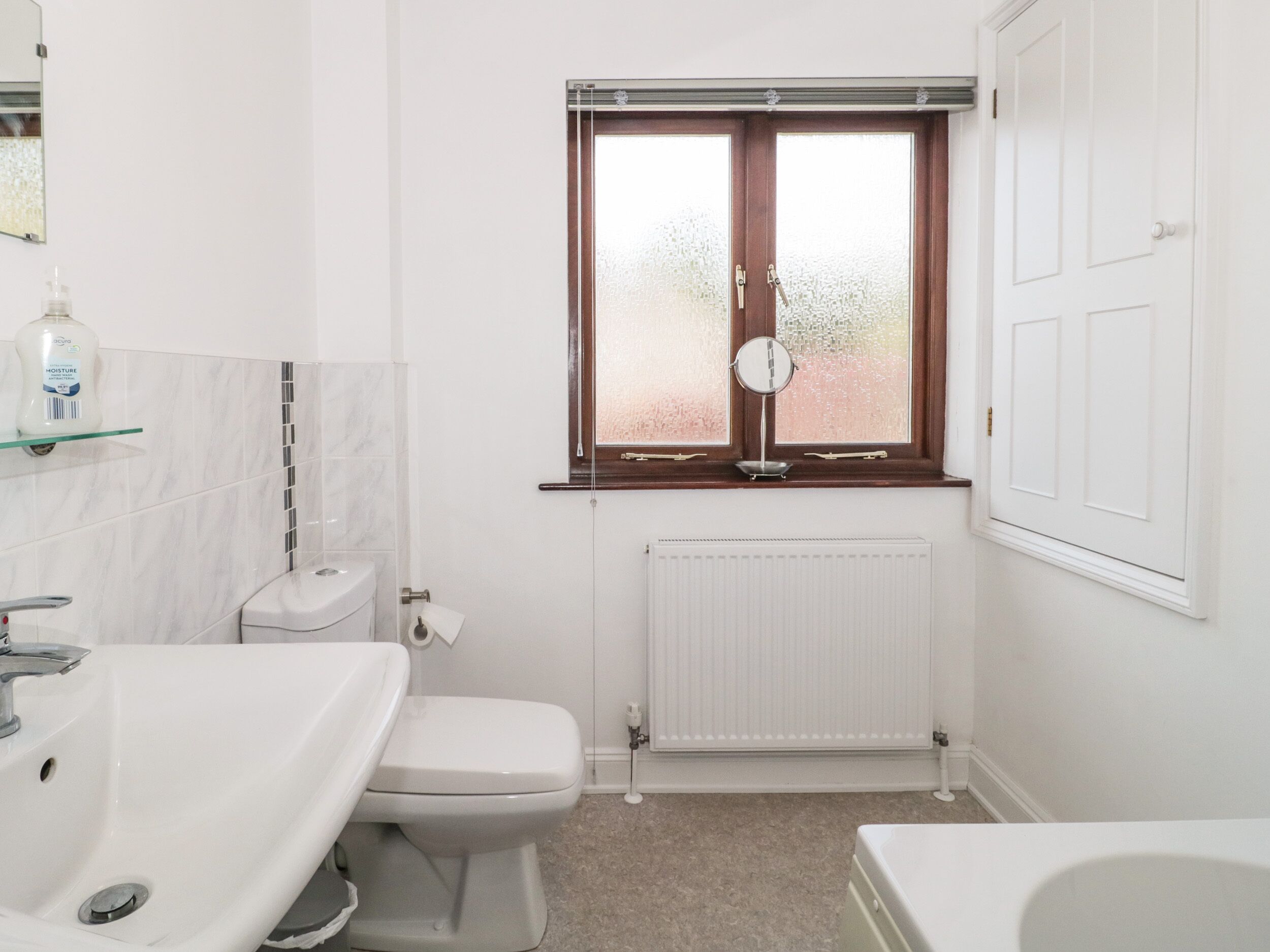 A bathroom with a toilet, a sink, a bathtub, a window with frosted glass, and a mirror.