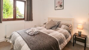 Un dormitorio con cama, lámpara de noche, ventana con cortinas, radiador y un cuadro en la pared.
