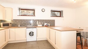 Cocina compacta con microondas, lavadora y lavaplatos. Hay dos ventanas y un reloj en la pared.
