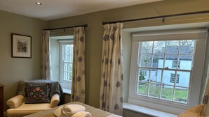 A bedroom with a bed, two windows, a chair, and a small table.