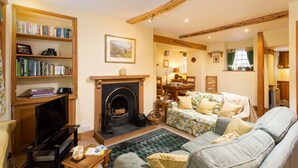 A cozy living room with a fireplace, a bookshelf, a floral sofa, and a dining area.
