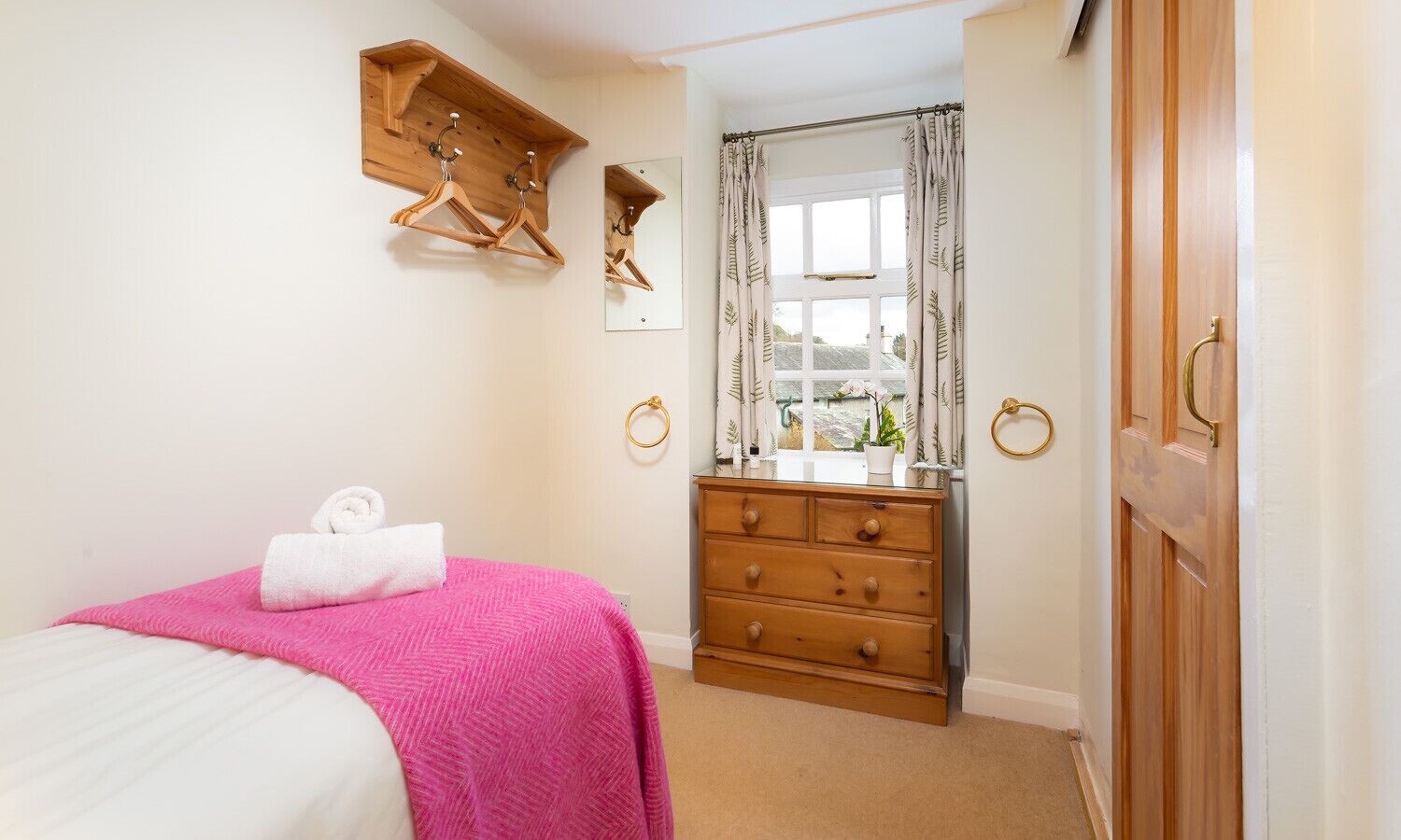 A bedroom with a bed, a dresser, a mirror, and a window with curtains.