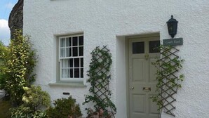 A two-story white building with a green door, windows, and a small garden with plants and flowers.