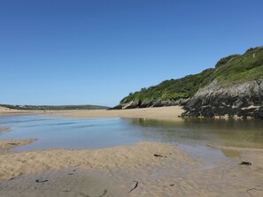A beach with clear water, sandy shore, and a rocky cliff with vegetation. - Great Western Farmhouse (Newquay)