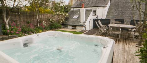 A hot tub in a backyard with a wooden deck, a table, and chairs.