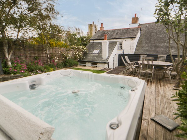 A hot tub in a backyard with a wooden deck, a table, and chairs.