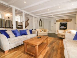 Un salón espacioso con una mesa de centro de madera, un sofá color beige con cojines azules y un sillón blanco.