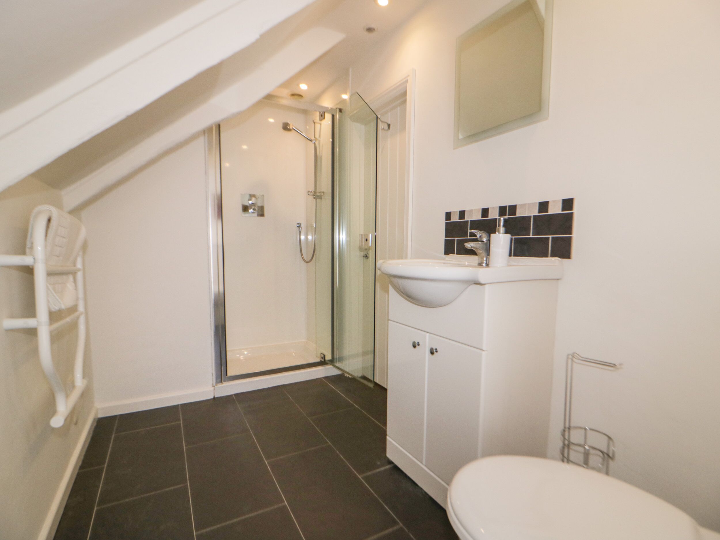 A modern bathroom with a glass-enclosed shower, a white sink, and a toilet.