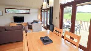 Un vaste espace de vie comprenant une table à manger en bois, des sièges confortables, un téléviseur et une grande fenêtre donnant sur l’extérieur.