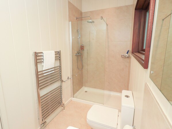 A bathroom with a glass shower enclosure, a towel rack, a toilet, and a window with a wooden frame. - Thie Loghey (Ambleside)