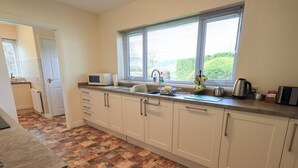 A kitchen with white cabinets, a tiled floor, a window with blinds, and various kitchen appliances. - Laal Field House (Keswick)