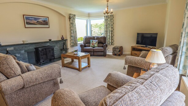 A cozy living room with a fireplace, leather sofa, and a television. - Laal Field House (Keswick)