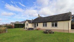 A house with a large lawn, a patio with a table and chairs, and a garage. - Laal Field House (Keswick)