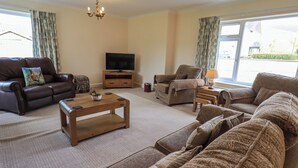 A living room with a brown leather sofa, a wooden coffee table, and a television on a stand. - Laal Field House (Keswick)