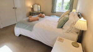 A neatly made bed with rolled towels, a bedside lamp, and a small table with a decorative item. - Laal Field House (Keswick)