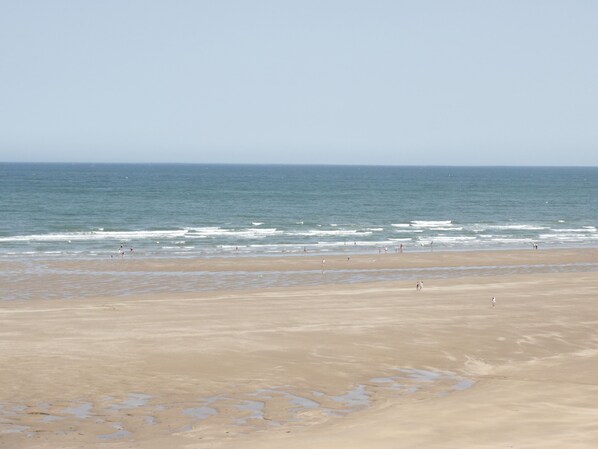 A wide beach with a clear view of the ocean and a few people walking along the shore.