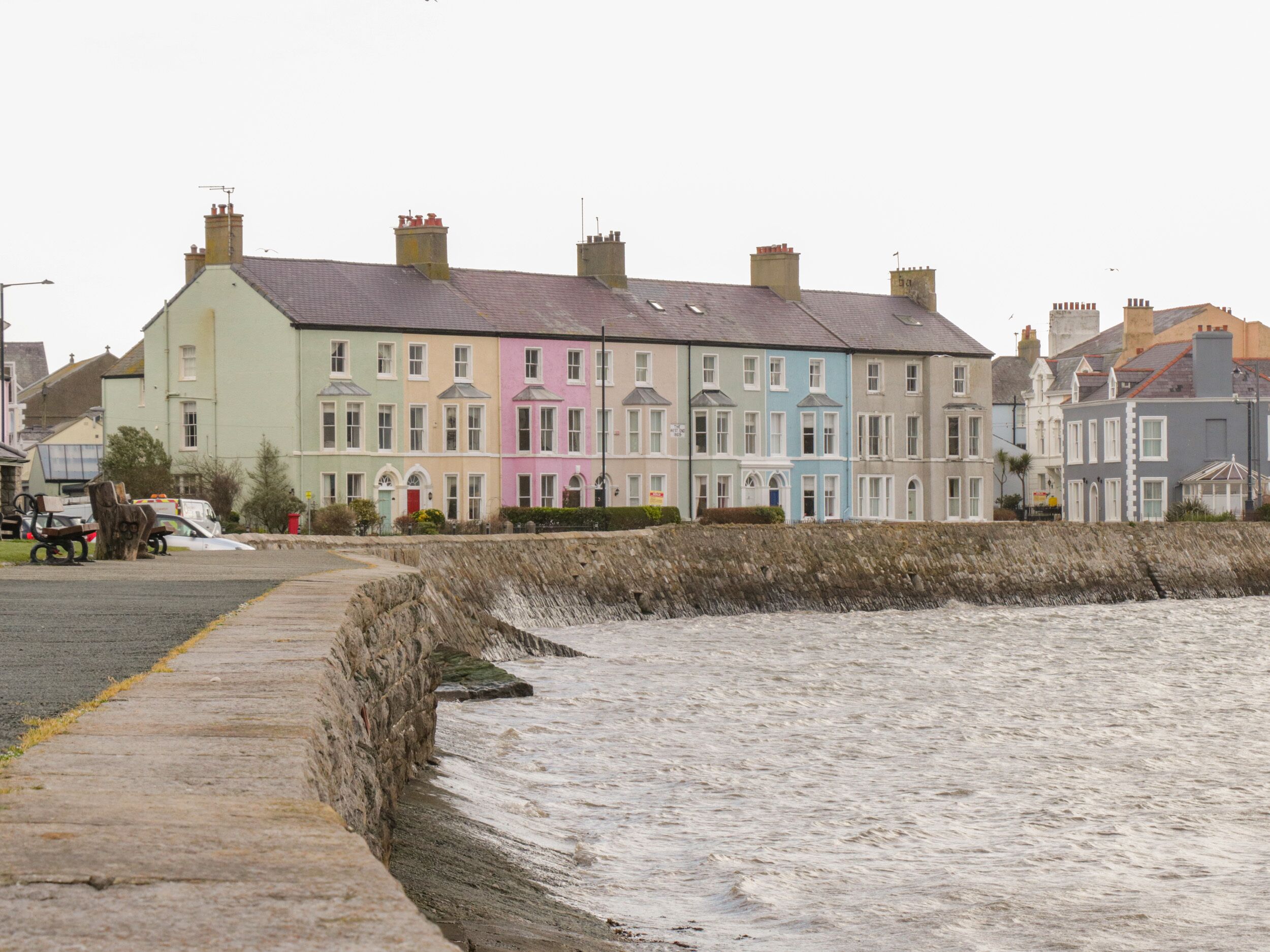 A row of colorful terraced houses by a rocky sea wall.