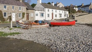 A coastal building with a stone facade, a red boat, and a white boat on a pebbled beach. - Banadlen Lodge (Brynteg)