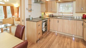 A modern kitchen with wooden cabinets, a built-in oven, and a dining area with a table and chairs. - Banadlen Lodge (Brynteg)