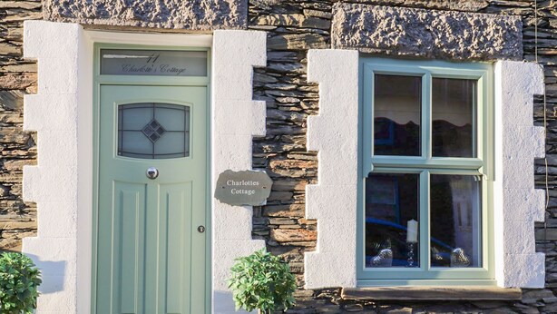 Ein Cottage mit grüner Tür, einer Steinmauer und einem Fenster mit Blick ins Innere.