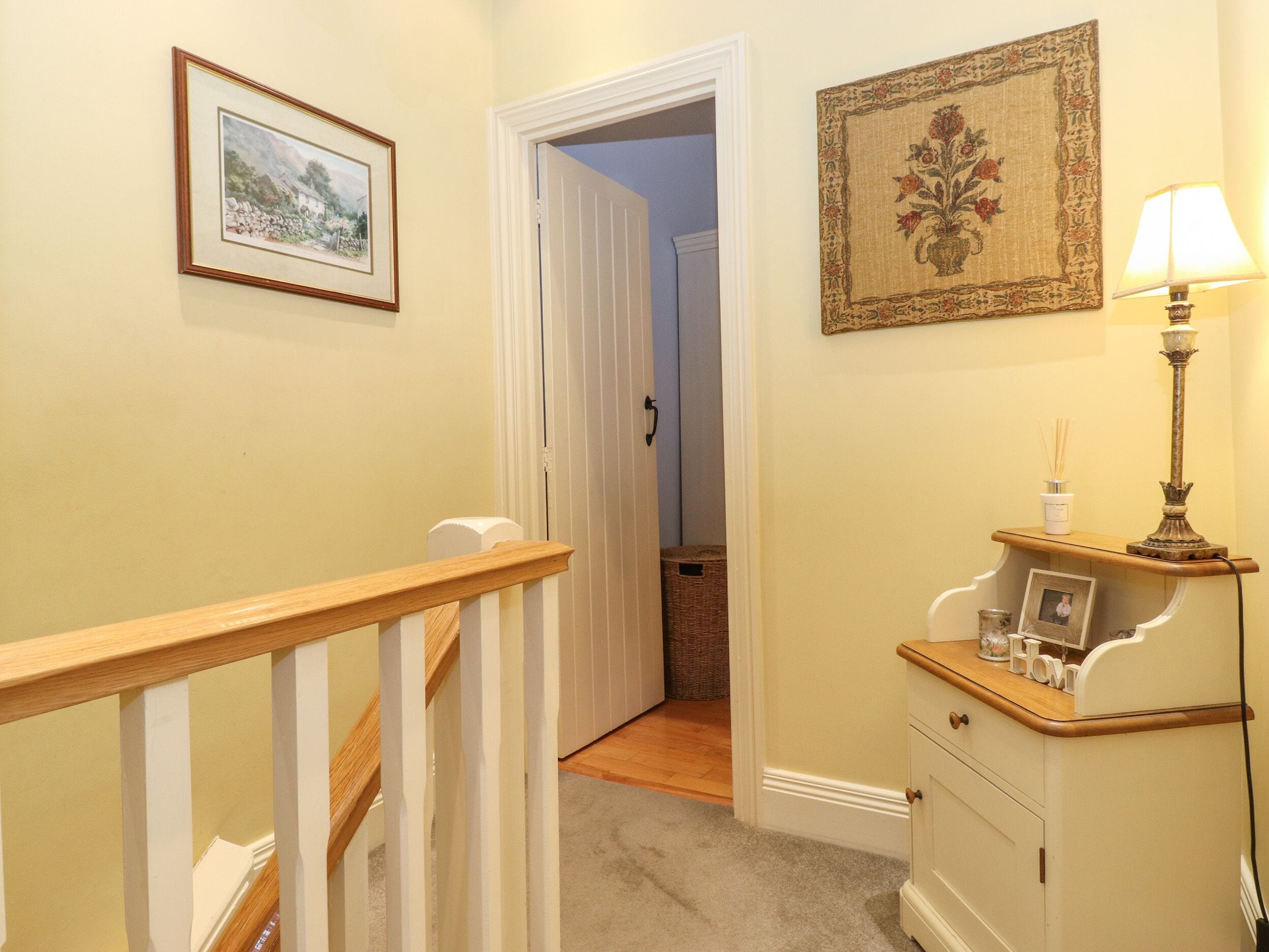 Un pasillo con una escalera de madera, un cuadro enmarco, una lámpara y un mueble bajo con un marco de fotos.