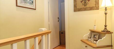 Un pasillo con una escalera de madera, un cuadro enmarco, una lámpara y un mueble bajo con un marco de fotos.