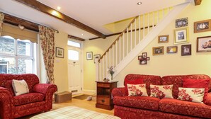 Ein gemütliches Wohnzimmer mit zwei roten Sofas, einem karierten Hocker und einer Holztreppe.