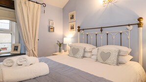 Ein Schlafzimmer mit Bett, Kissen, Nachttisch, Lampe und einem Fenster mit Vorhängen.