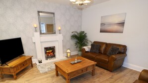 A living room with a fireplace, a TV, a brown leather sofa, and wooden furniture. - The Coach House (Bradford)