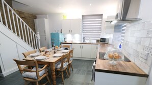 A modern kitchen with a dining area, featuring a wooden table and chairs, a blue refrigerator, and a microwave. - The Coach House (Bradford)