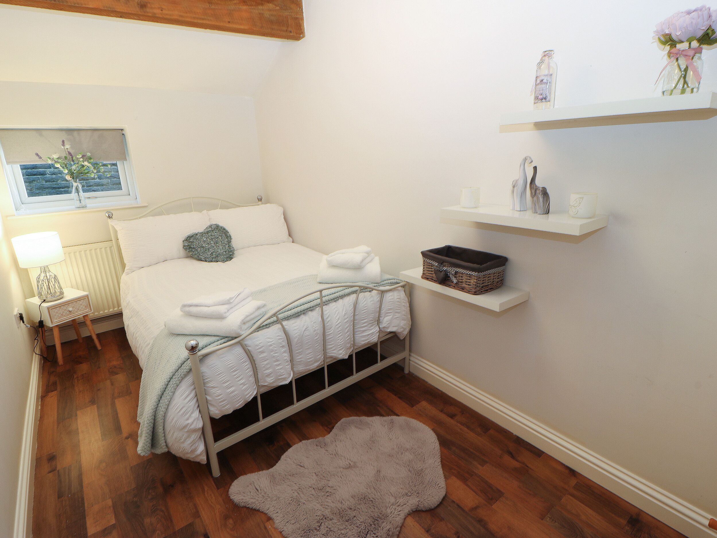A neatly arranged bedroom with a bed, bedside table, lamp, and a small rug.