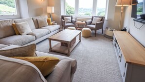 Ein gemütliches Wohnzimmer mit einer Couch, Sesseln, einem Couchtisch und einem Fernseher.