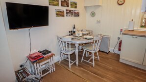 A small, cozy kitchen with a dining table, chairs, and a TV mounted on the wall. - Winskill Cottage (Settle)