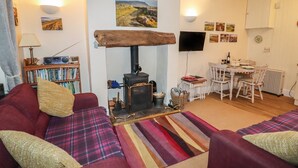 A cozy living room with a sofa, a fireplace, a television, and a dining area with a table and chairs. - Winskill Cottage (Settle)