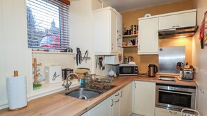 A compact kitchen with white cabinets, a stainless steel sink, a microwave, a toaster, and a stove. - Winskill Cottage (Settle)