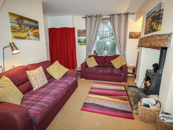 A cozy living room with two red sofas, a fireplace, and a window with curtains. - Winskill Cottage (Settle)