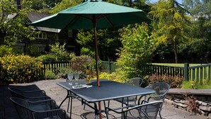 An outdoor patio with a table and chairs, a green umbrella, and a stone wall. - The Old Barn (Windermere)