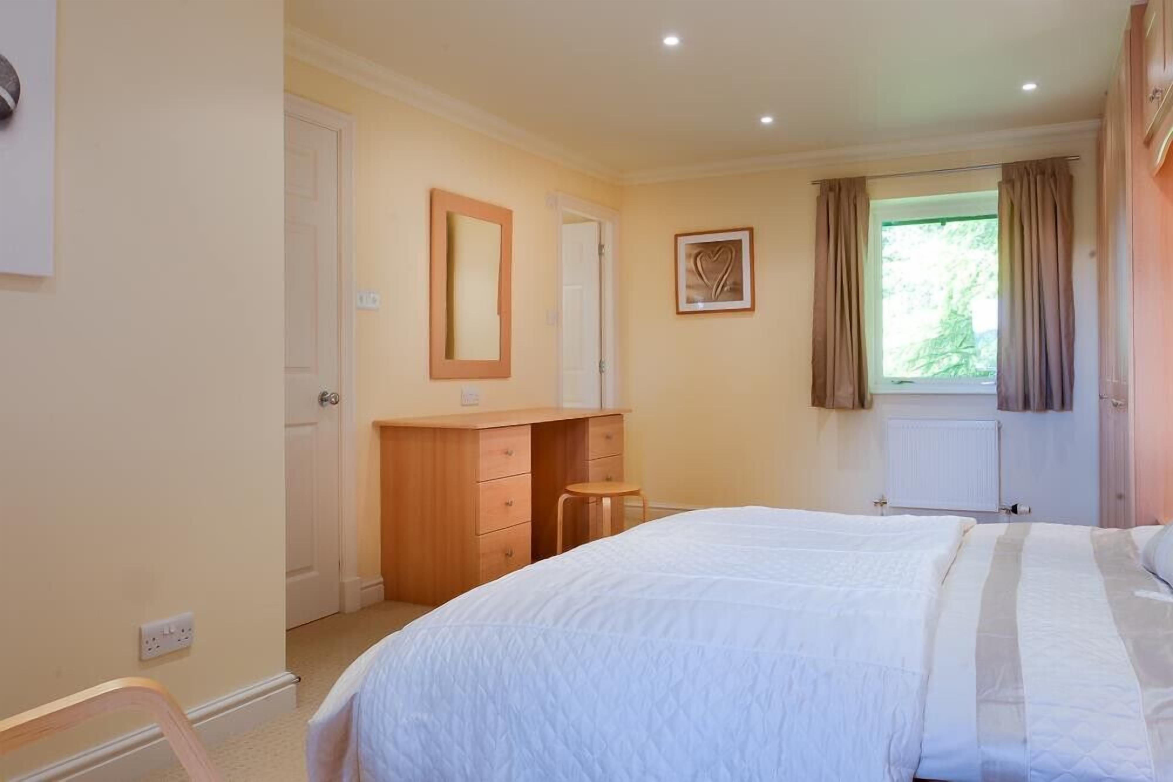 A bedroom with a bed, a wooden dresser, a mirror, and a window with curtains.