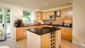 A modern kitchen with wooden cabinets, a central island, and a large window providing natural light. - The Old Barn (Windermere)