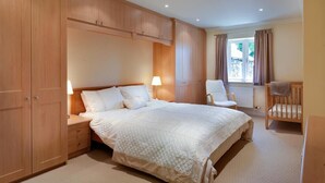 A bedroom with a large bed, wooden wardrobe, a chair, and a window with curtains. - The Old Barn (Windermere)