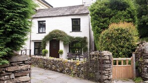 A white building with a dark brown door, stone walls, and a wooden gate. - Burrow Cottage (Windermere)