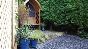 A wooden structure with a window, surrounded by lush greenery and potted plants. - Burrow Cottage (Windermere)
