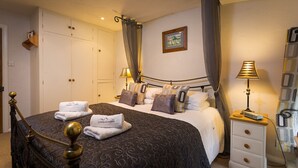 A bedroom with a bed, two bedside tables, a wardrobe, and a picture on the wall. - Burrow Cottage (Windermere)