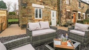 A stone house with a patio area featuring wicker furniture and a glass table with a tray. - 1 Town Head (Buxton)