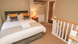 A neatly made bed with pillows, a bedside lamp, and a rolled towel on the floor. - 1 Town Head (Buxton)