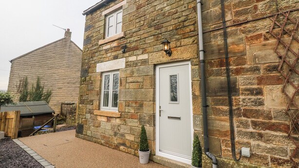 A stone house with a white door, a window, and a small garden area with gravel and potted plants. - 1 Town Head (Buxton)