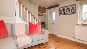 A living room with a grey sofa, red and pink cushions, wooden flooring, a staircase with white railings, and a framed cow picture on the wall. - 1 Town Head (Buxton)