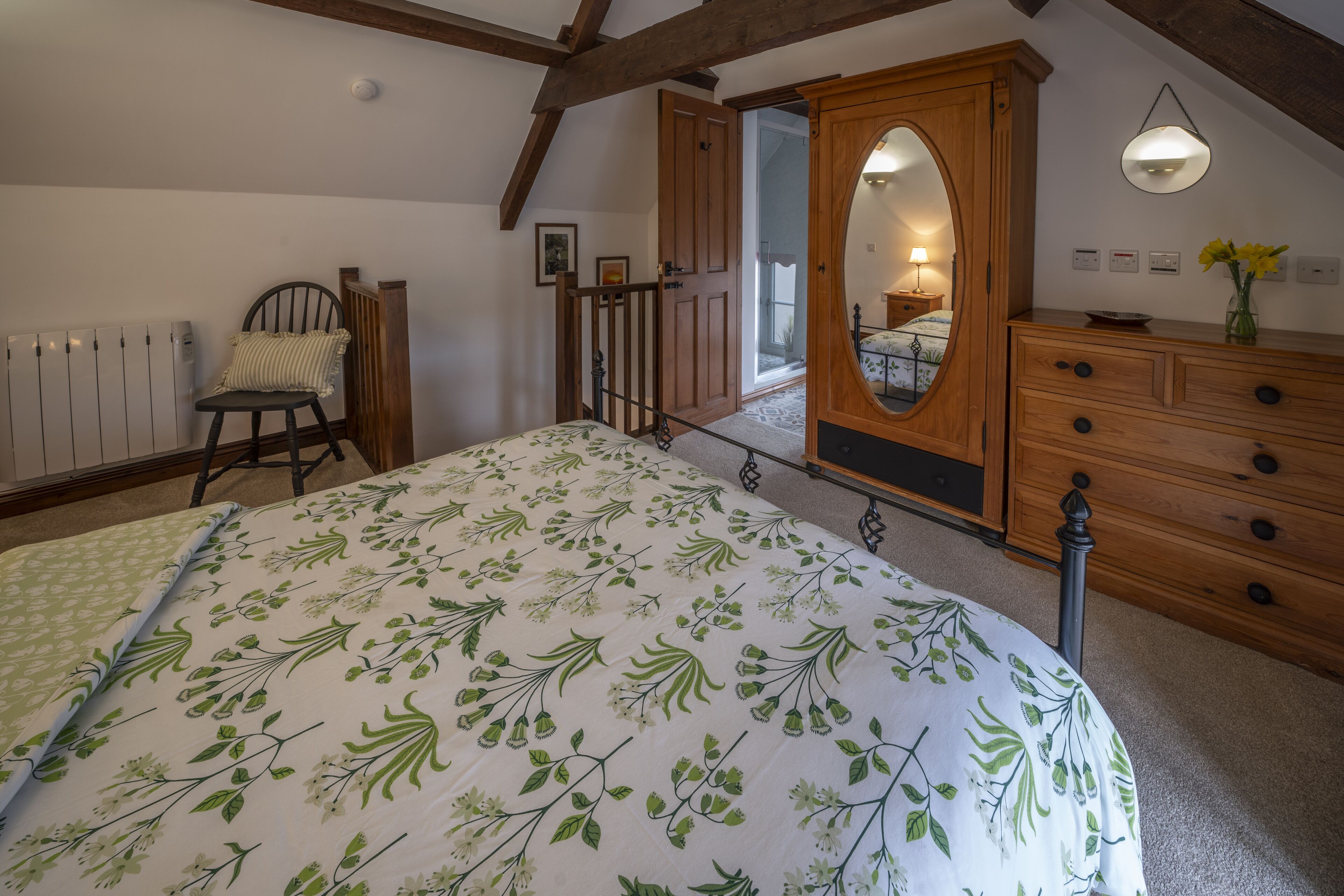 A bedroom with a bed, wooden dresser, and a mirror.