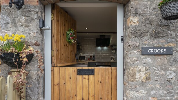 A rustic wooden door with a sign reading "CROOKS" and a stone wall. - Crooks (Axbridge)