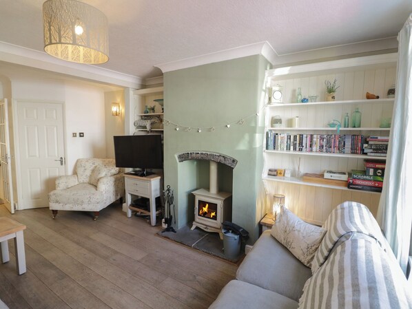 A cozy living room with a fireplace, a television, a bookshelf, and a patterned sofa. - Heath Cottage (Stratford-upon-Avon)